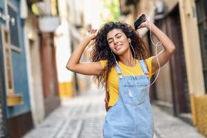 atractiva chica africana escuchando música con auriculares al aire libre. foto