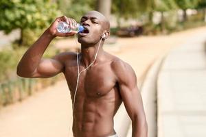 hombre negro bebiendo agua después de correr en el fondo urbano. foto