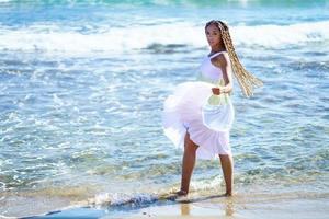 mujer negra caminando por la orilla de la playa con un hermoso vestido largo.