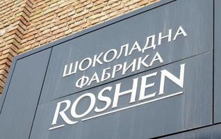 The main entrance to the building of the Roshen confectionery chocolate factory in Kiev. White letters in Ukrainian on a black sign. Emblem of the Roshen company. Ukraine, Kiev - February 09, 2022. photo