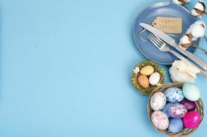 Festive Easter table setting with painted eggs on blue background. Space for text. Studio Photo