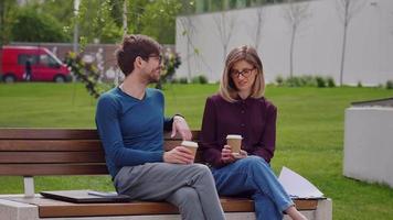 Zwei Freunde mit Brille sitzen auf der Bank und schlürfen Kaffee zum Mitnehmen. Kaffeepause.