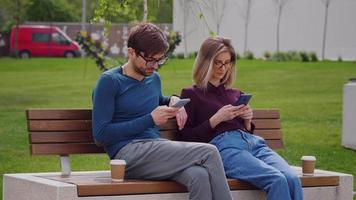 pareja de amigos que usan teléfonos inteligentes en el parque al aire libre. video