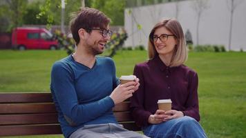 Two friends with glasses, sit on the bench while sipping coffee to-go Coffee Break video
