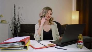 vrouw die op laptop in het kantoor aan huis werkt en een financieel document bespreekt met collega's via een telefoontje. video