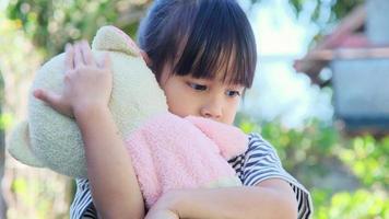 linda niña sosteniendo y abrazando a su muñeca. niños jugando con juguetes de peluche en el patio delantero. video