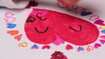 close-up de uma menina desenhando um coração e colorindo com seus marcadores coloridos. linda jovem fazendo lição de casa na mesa em casa. Artes e Ofícios.