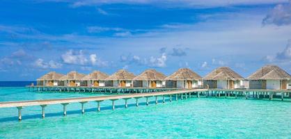 Overwater bungalows in the Indian Ocean, Maldives islands. Tropical ocean lagoon, turquoise water, idyllic cloudy sky. Summer vacation, holiday, traveling destination photo