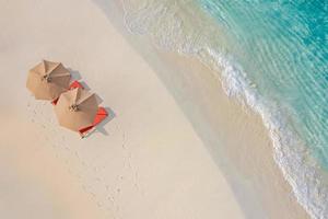 Aerial view of amazing beach with umbrellas and lounge chairs beds close to turquoise sea. Top view of summer beach landscape, idyllic inspirational couple vacation, romantic holiday. Freedom travel