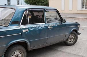 Old damaged car parked on an empty street in Tomsk, Siberia. Blue color, no people. photo