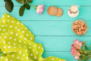 Frame of morning food with jug of milk, cookies and oat-flakes on blue wooden background. Tablecloth in polka dots and flowers. Top view. Mock up. Copy space photo
