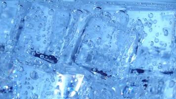 cubos de gelo com bolhas de ar giram no copo. soda e resfrie em um copo transparente. video