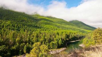 Time lapse clouds travel over a river and forested hillside. video