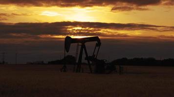 pomp jack. oliebron. pomp jack. oil well.silhouette van een oliepomp jack op rig als de zon op de achtergrond ondergaat. een oliepompkrik in het midden van het tarweveld met de prachtige zonsonderganghemel. video