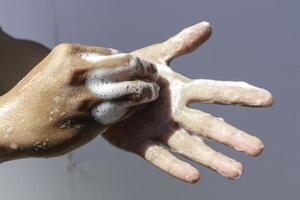 el hombre usa jabón y se lava las manos con fondo gris bajo la luz del sol. detalle de la mano del concepto de higiene foto