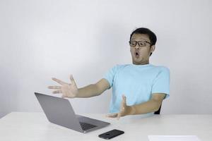 Wow face of Young Asian man shocked what he see in the laptop when working isolated grey background wearing blue shirt. photo