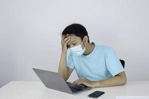 el joven asiático que usa una máscara médica no se siente saludable, cansado y confundido con trabajar en computadoras portátiles en la mesa.