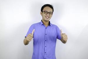 joven asiático usa camisa azul y anteojos con cara sonriente feliz y pulgares hacia arriba