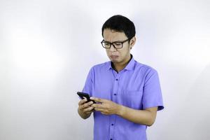 Young Asian man cry and sad when looking and using phone. Indonesia Man wear glasses and blue shirt Isolated blue background. photo