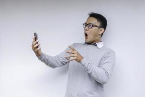 wow, la cara de tu hombre asiático se sorprendió por lo que vio en el teléfono inteligente con un fondo gris aislado. foto