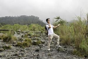 Young asian backpacker man is happy and smile when he looking smartphone in mountain traveling photo