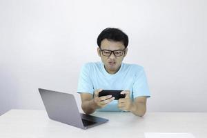 Angry Asian young man get mad on the smartphone when play game at work. Indonesian man wearing blue shirt. photo