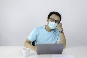 Young Asian man wearing medical mask is feeling unhealthy, tired, and confuse with work in laptop. photo