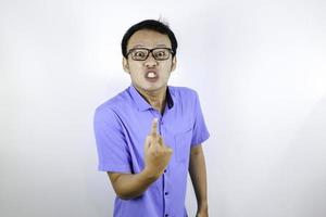 Young Asian Man wear blue shirt is funny angry face with shouting and pointing finger at camera isolated over white background photo