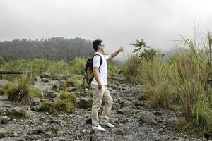 el joven mochilero asiático es feliz y disfruta viajando en la montaña foto