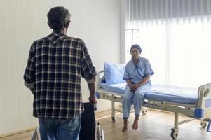 Senior man helping cancer patient woman wearing head scarf moving to wheelchairs at hospital, health care and medical concept photo