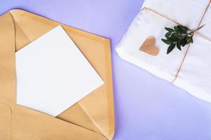 Opened craft paper envelope with empty white paper, gift in eco package with green twigs from above on very pari back. photo