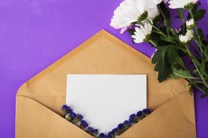 Opened craft paper envelope with empty piece of paper and dried blue flowers and white flowers near on very peri background photo