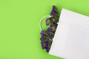 Blue, dried flowers in white paper bag on the green background.. Close up. Top view, copy space photo