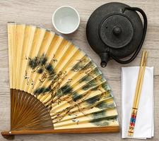 Juego de té de cultura oriental con palillos y abanico plegable sobre fondo de madera. foto