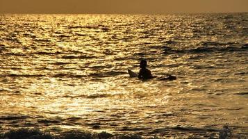 Documentation of surfers in action at dusk with a golden color and dark, unfocused and dark on the beach of Senggigi Lombok, West Nusa Tenggara Indonesia, 27 November 2019 photo