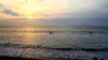 Documentation of surfers in action at dusk with a golden color and dark, unfocused and dark on the beach of Senggigi Lombok, West Nusa Tenggara Indonesia, 27 November 2019 photo