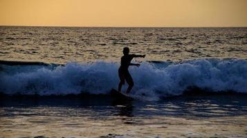 Documentation of surfers in action at dusk with a golden color and dark, unfocused and dark on the beach of Senggigi Lombok, West Nusa Tenggara Indonesia, 27 November 2019 photo