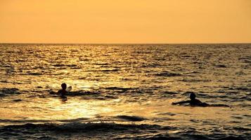 documentación de surfistas en acción al atardecer con un color dorado y oscuro, desenfocado y oscuro en la playa de senggigi lombok, oeste de nusa tenggara indonesia, 27 de noviembre de 2019 foto