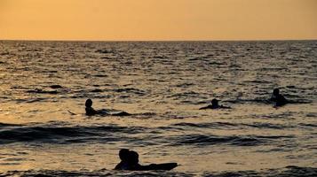 Documentation of surfers in action at dusk with a golden color and dark, unfocused and dark on the beach of Senggigi Lombok, West Nusa Tenggara Indonesia, 27 November 2019 photo