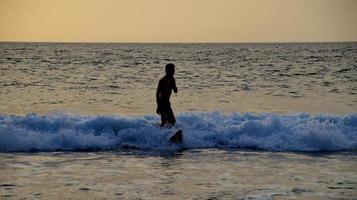 documentación de surfistas en acción al atardecer con un color dorado y oscuro, desenfocado y oscuro en la playa de senggigi lombok, oeste de nusa tenggara indonesia, 27 de noviembre de 2019 foto