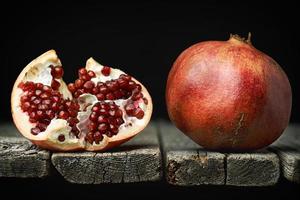 Ripe pomegranate with a half with red seeds on the edge of old rough wooden boards photo