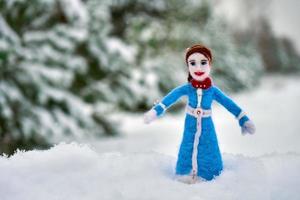 muñeca de lana de fieltro de aguja en la nieve con pinos nevados en el fondo foto