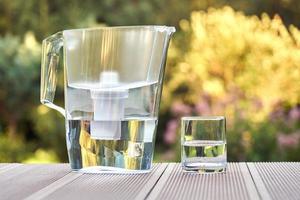 Water filter pitcher and a clean glass of a clear water close up on the summer garden background photo