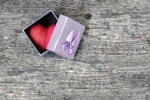 Red wool toy heart lying in a open gift box on a wooden table. Heart as a gift. photo