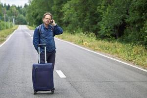 Man with a luggage standing in the middle of a asphalt road and speaks on mobile phone photo