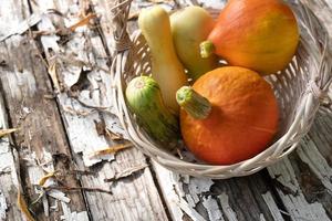 Still life with pumpkins and zucchinis in a wicker backet on the old wooden boards with a peeling paint and fallen autumn leaves photo