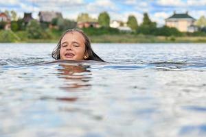 Smiling teenage girl swims in russian suburban lake in summer photo