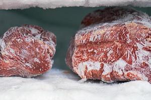 Large pieces of red meat in a freezer with a big quantity of frozen ice and snow photo