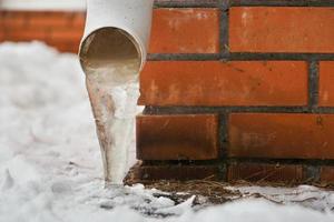 Drain pipe with frozen stream of water near house brick wall photo