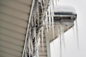 Icicles hanging on the roof of a cottage in winter or spring. House roof covered with big icicles. photo